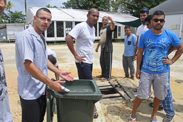 Asylum seekers are collecting water from a dirty makeshift well and filling rubbish bins