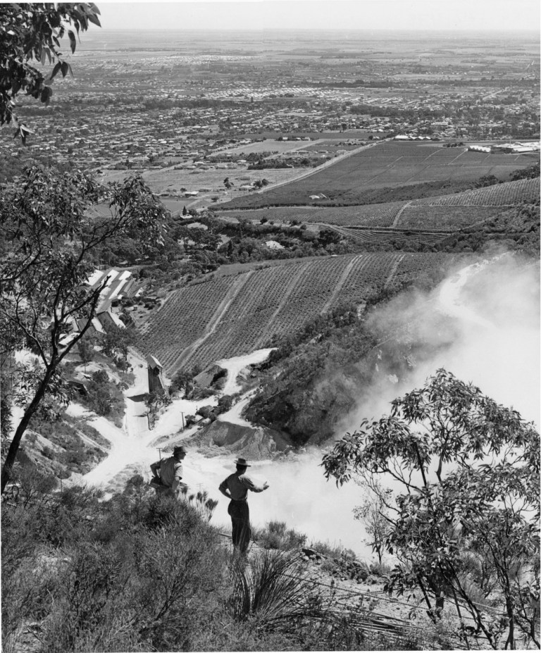 A charge is fired at the Stonyfell Quarries in the Hills above Adelaide. Looking out over Stonyfell Vineyards are Penfolds Magill Vineyards a vista of some of the N.E. suburbs is seen. The foreground quarrymen are 'New Australians'.